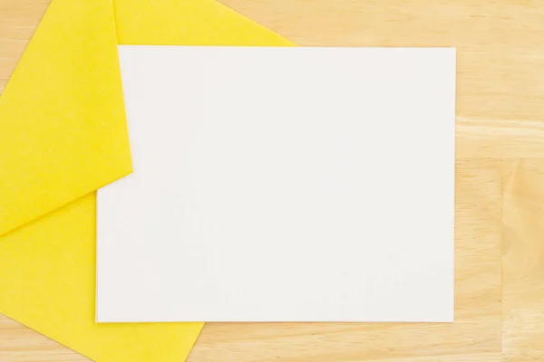 木製の机の上に黄色の封筒に空白の白いグリーティングカード — ストック写真