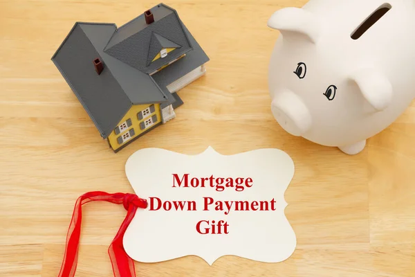 Mortgage down payment gift message on a gift tag with a model house with a piggy bank on wood desk