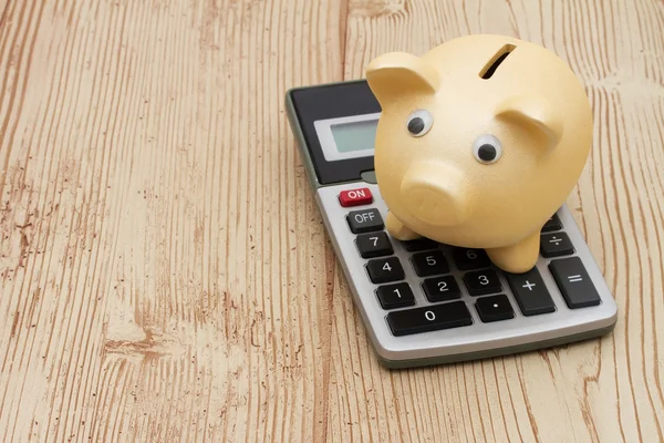 Een gouden piggy bank en Rekenmachine op hout achtergrond — Stockfoto