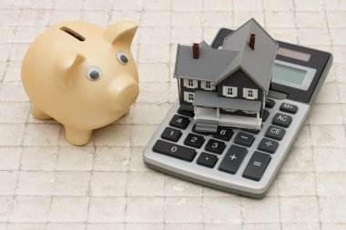 A gray house, piggy bank and calculator on stone background