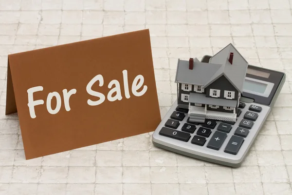 Para venda, uma casa cinza, cartão marrom e calculadora em backg de pedra — Fotografia de Stock