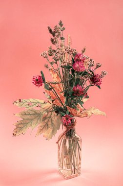 Pembe arka planda sonbahar çiçekleri olan şeffaf vazo