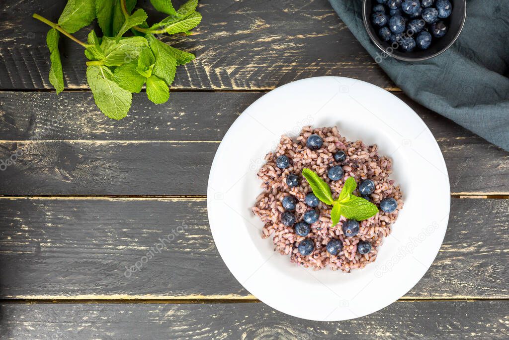 Delicious risotto with blueberries served on dark wooden table, flat lay