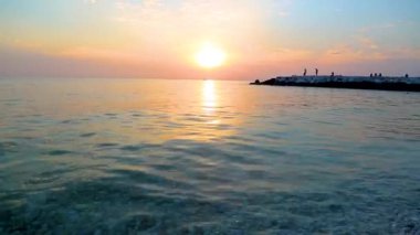 Deniz dalgaları üzerinde gün batımı taşları yıkar