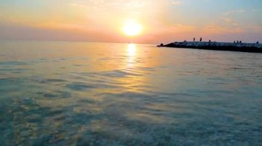 Deniz dalgaları üzerinde gün batımı taşları yıkar