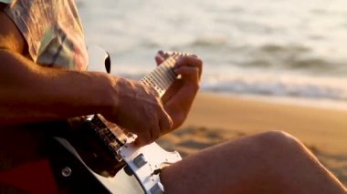 Gün batımında deniz kenarında gitar çalan adam.