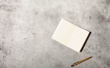 Açık satırlı defterleri ve somut arka planda izole edilmiş kalemi olan bir model.