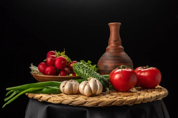 Still life with vegetables on a black background. Radishes, tomatoes, green onions, garlic, lettuce, cucumber.