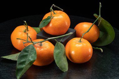 Siyah arka planda yaprakları olan mandalinalar..