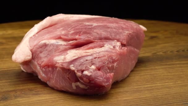 Un trozo de carne de cerdo fresca cruda sobre una superficie de madera — Vídeos de Stock