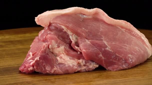 Un trozo de carne de cerdo fresca cruda sobre una superficie de madera — Vídeos de Stock