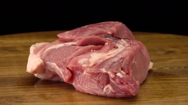 Un trozo de carne de cerdo fresca cruda sobre una superficie de madera — Vídeo de stock