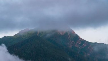 Hızla hareket eden bulutların arka planına karşı dağ zirveleri.