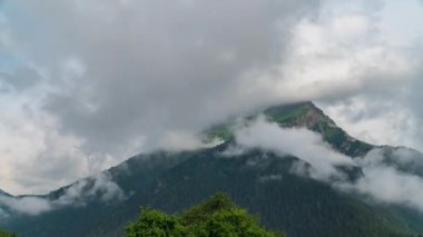 Hızla hareket eden bulutların arka planına karşı dağ zirveleri.