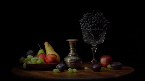 Natureza morta com frutas em uma mesa redonda de madeira e fundo preto. — Vídeo de Stock