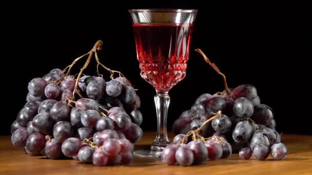 Copa con vino y uvas rojas oscuras sobre fondo negro — Vídeos de Stock