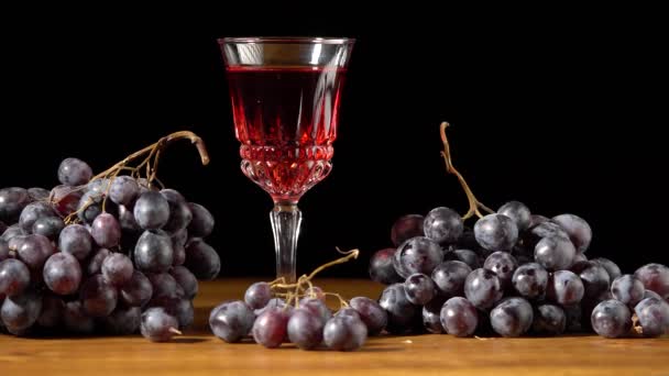 Copa con vino y uvas rojas oscuras sobre fondo negro — Vídeo de stock