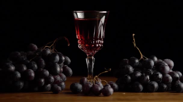 Copa con vino y uvas rojas oscuras sobre fondo negro — Vídeo de stock