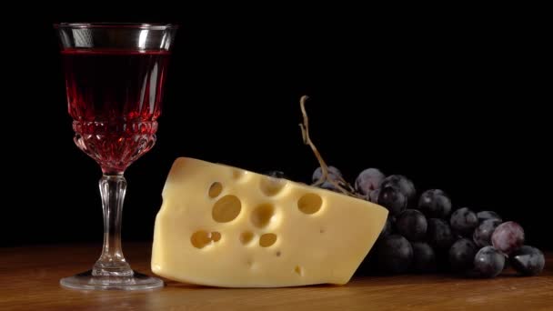 Pedazo de queso, vaso con vino y uvas sobre fondo negro — Vídeo de stock