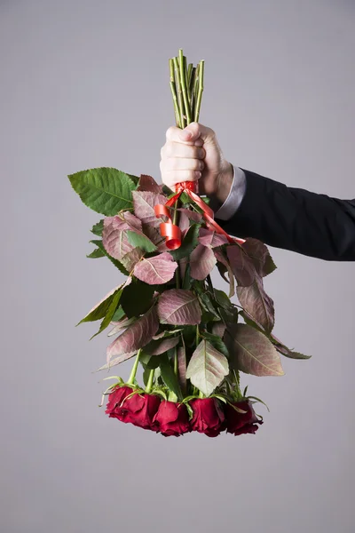 Man met boeket van rode rozen op een grijze achtergrond — Stockfoto