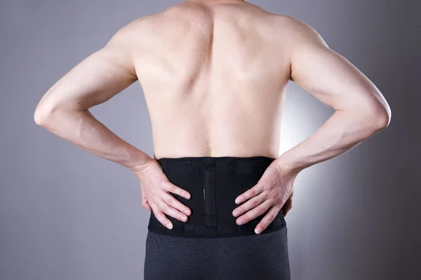 Bărbat cu centură medicală pentru spate pe un fundal gri — Fotografie, imagine de stoc