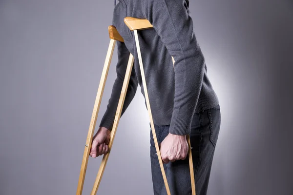 Man op krukken op een grijze achtergrond — Stockfoto