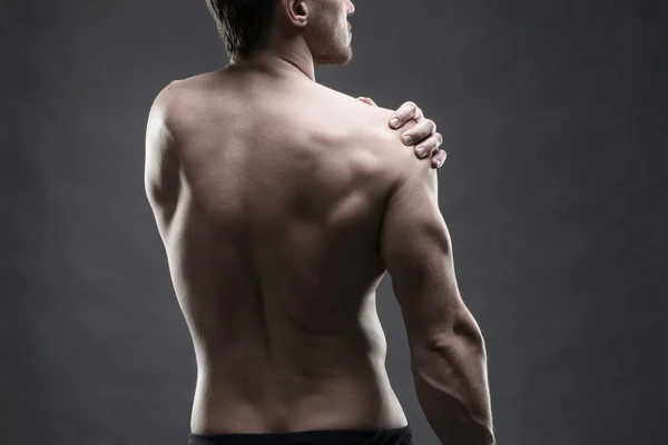 Dolor en el hombro. Cuerpo masculino muscular. Guapo culturista posando sobre fondo gris. Llave baja de cerca plano de estudio —  Fotos de Stock