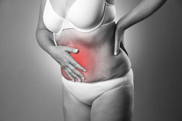 Mujer con sostén blanco y bragas blancas con dolor abdominal sobre un fondo gris. Estudio filmado con punto rojo — Foto de Stock