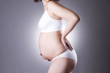 Caucasian pregnant woman in white lingerie with back pain on gray studio background clipart