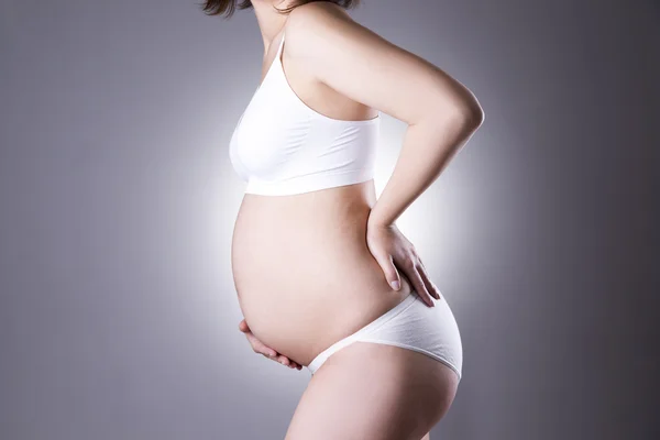 Kaukasische zwangere vrouw in witte lingerie met rugpijn op grijze studio achtergrond — Stockfoto