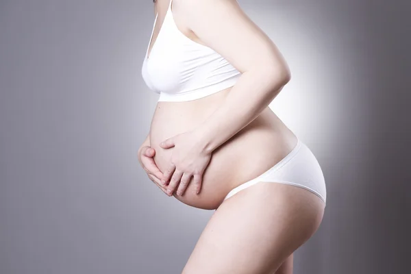 Caucasian pregnant woman in white lingerie with abdominal pain on gray studio background — Stock Photo, Image