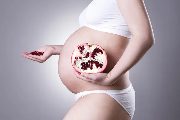 Pregnancy and nutrition - pregnant woman with pomegranate in hand on gray background — Stock Photo, Image