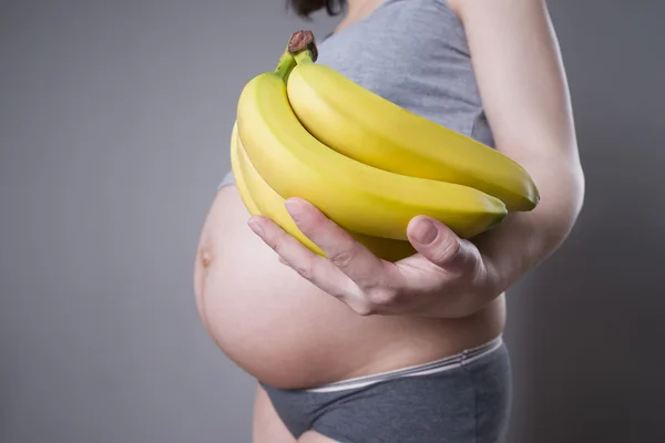 Pregnancy and nutrition - pregnant woman with bananas in hand on gray background — Stock Photo, Image