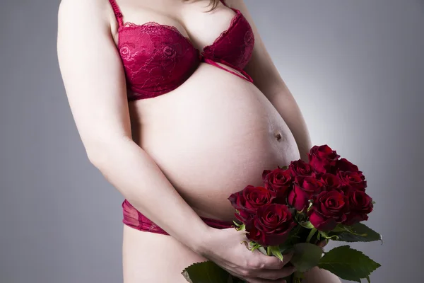 Genç güzellik ve seksi beyaz hamile kadın ile gri arka plan üzerinde kırmızı gül buketi — Stok fotoğraf