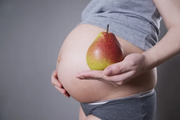 Gebelik ve beslenme - gri arka plan üzerinde elinde armut ile hamile kadın — Stok fotoğraf