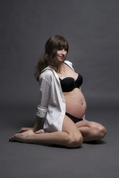 Jeune beauté et sexy femme enceinte caucasienne en lingerie noire sur fond de studio gris — Photo