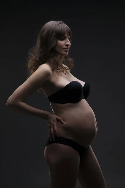 Молодая красавица и сексуальная белая беременная женщина в черном нижнем белье на сером фоне студии — стоковое фото