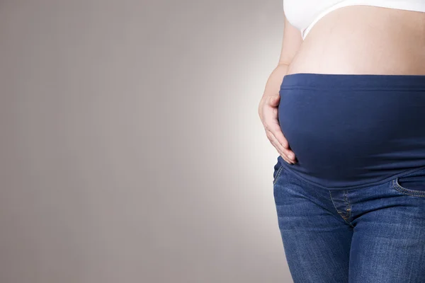 Mujer embarazada en jeans azules para mujeres embarazadas sobre fondo gris. Copiar espacio — Foto de Stock