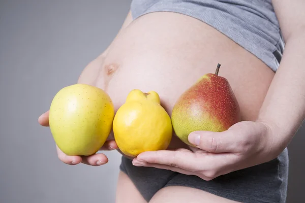 Pregnancy and nutrition - pregnant woman with fruits in hand on gray background — Stock Photo, Image