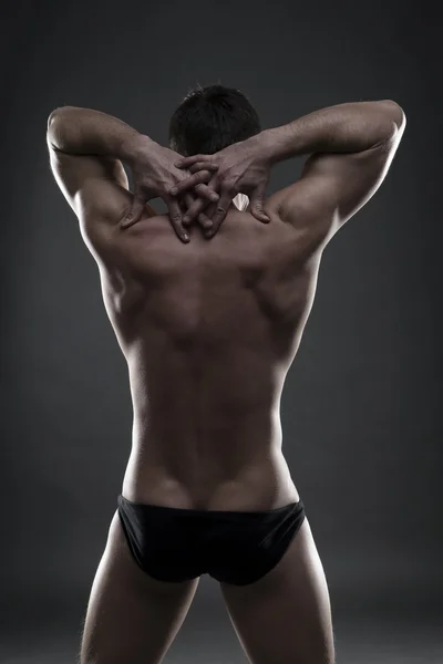 Handsome muscular bodybuilder posing on gray background. Low key studio shot — Stock Photo, Image