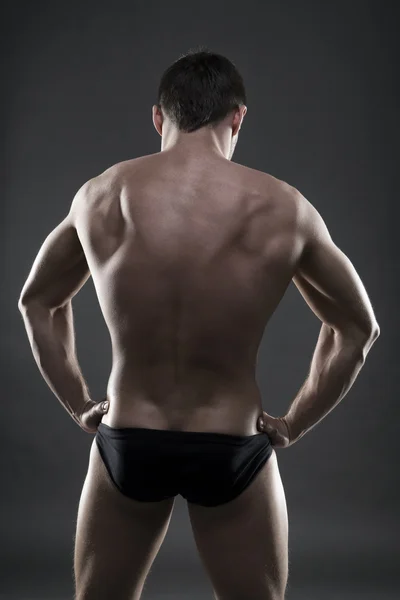 Bonito fisiculturista muscular posando em fundo cinza. Baixo tiro estúdio chave — Fotografia de Stock