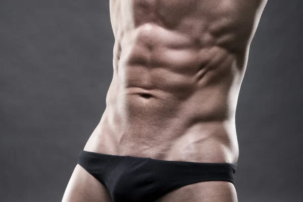 Bello bodybuilder muscolare in posa su sfondo grigio. Basso tasto close up studio girato — Foto Stock
