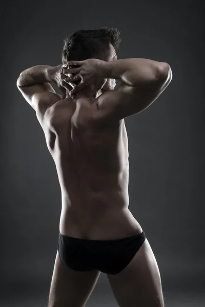 Handsome muscular bodybuilder posing on gray background. Low key studio shot — Stock Photo, Image