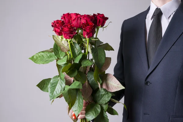 Hombre con ramo de rosas rojas sobre un fondo gris — Foto de Stock