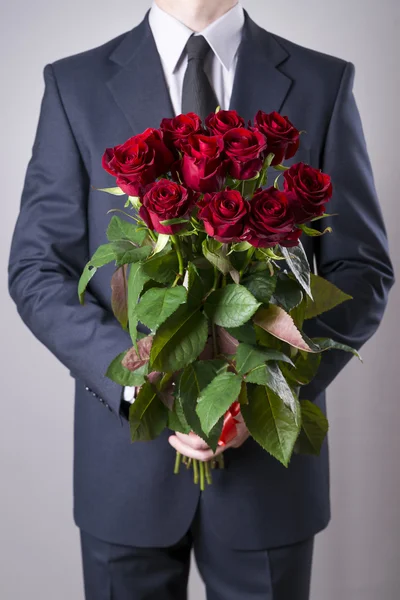 Hombre con ramo de rosas rojas sobre un fondo gris — Foto de Stock