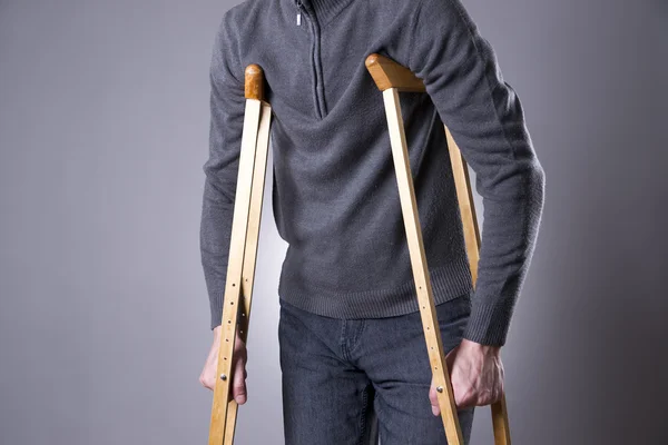 Hombre con muletas sobre un fondo gris —  Fotos de Stock