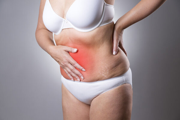 Woman in a white bra and white panties with abdominal pain on a gray background. Studio shot with red dot