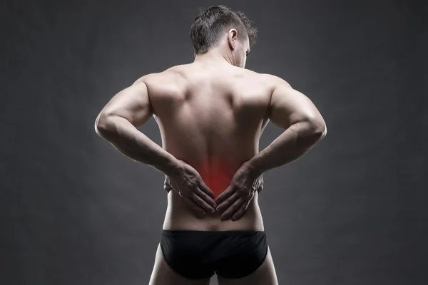 Nierenschmerzen. Mann mit Rückenschmerzen. schöner muskulöser Bodybuilder, der auf grauem Hintergrund posiert. Low-Key Nahaufnahme Studioaufnahme — Stockfoto