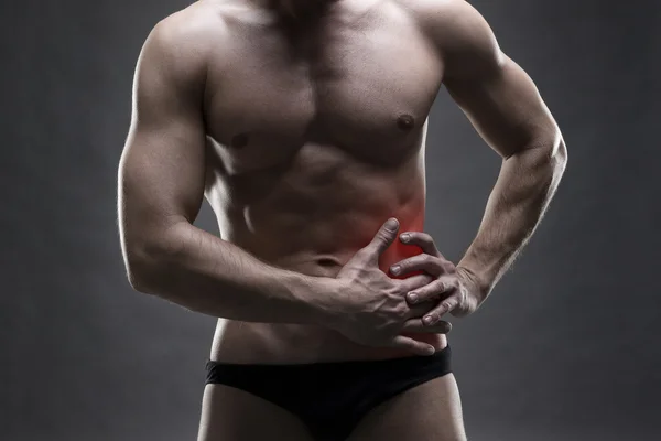 Pain in the left side. Muscular male body. Handsome bodybuilder posing on gray background — Stock Photo, Image