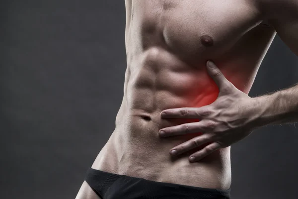 Dolor en el lado izquierdo. Cuerpo masculino muscular. Guapo culturista posando sobre fondo gris — Foto de Stock